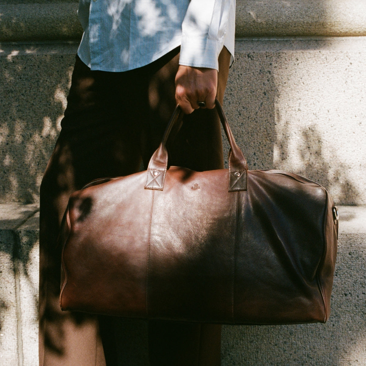 Man holding brown leather weekend bag