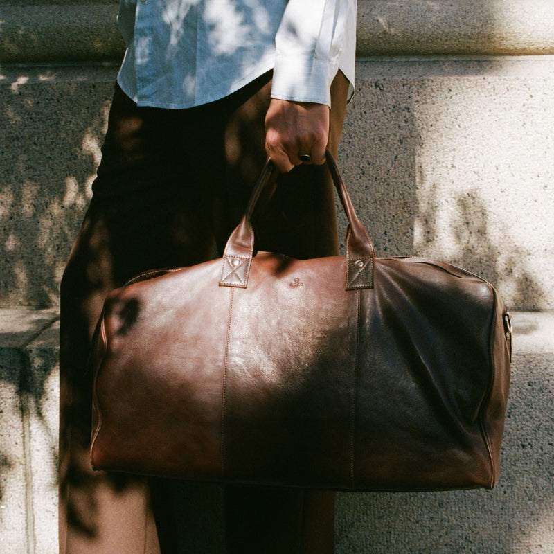 Man holding brown leather weekend bag